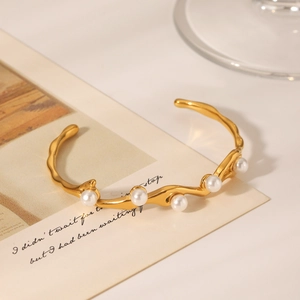Dettaglio di un bracciale rigido in acciaio dorato con cinque eleganti perle bianche