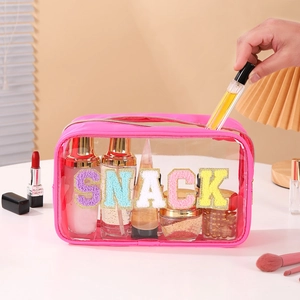 Detail of transparent PVC toiletry bag showing colorful glitter SNACK letter patches
