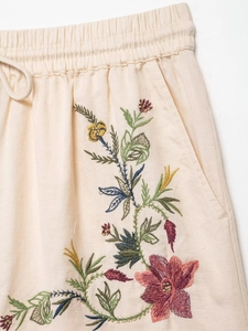 Detail of drawstring waist and colorful floral embroidery on beige knit shorts