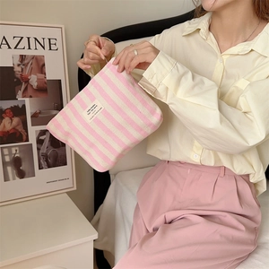 Pink and white striped canvas makeup bag held by a model in a cozy lifestyle setting