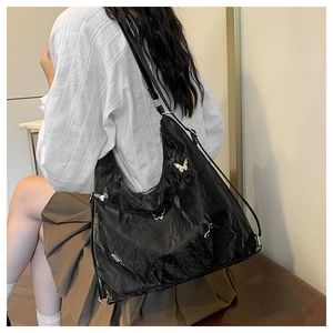 Detail of black pleated tote bag with silver butterfly charms worn by a model