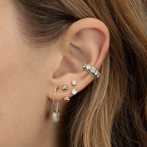 Close-up of gold tassel earrings and zircon ear cuffs worn by a model in detail