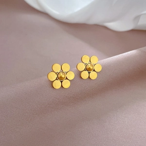 Detailed view of golden six-leaf flower stud earrings on soft pink satin fabric