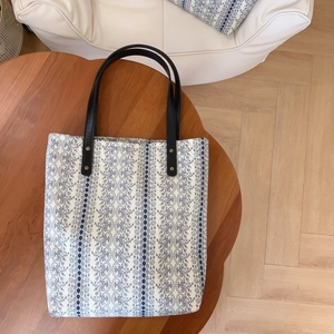 Detail of floral tote bag with blue patterns, leather handles and rivet accents