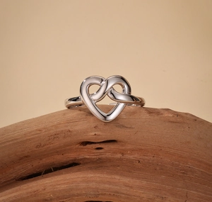Macro shot of silver heart knot ring resting on a textured natural wood surface