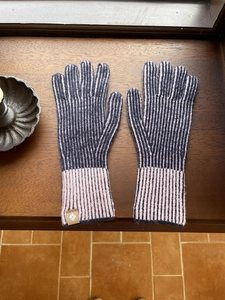 Detalle de guantes de punto a rayas grises y rosas con puños sobre base de madera