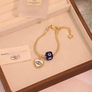 Gold snake chain bracelet featuring blue cubic evil eye and white heart charms