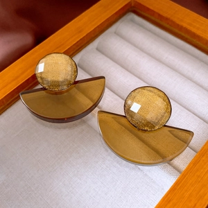 Close-up of geometric resin earrings with gold foil and amber tones in a jewelry box