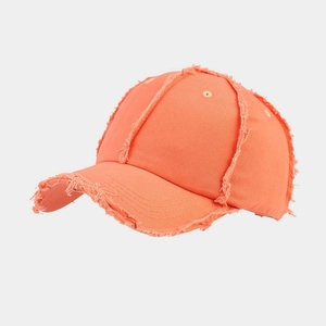 Detail of bright orange distressed baseball cap showing raw edges and cotton canvas texture