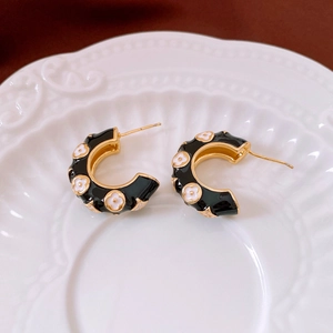 Close-up of C-shaped gold-plated hoop earrings with black enamel and white flowers