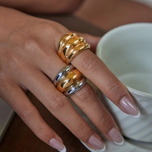 Close-up of chunky gold and silver dome rings worn on hand holding a coffee cup