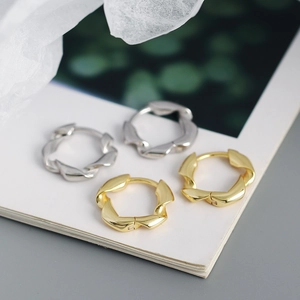 Macro shot of twisted metal huggie earrings in polished gold and silver finishes