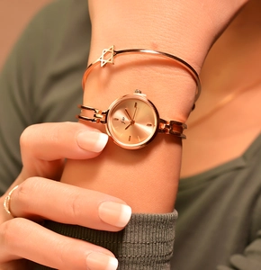 Close-up of rose gold watch with small dial and matching star charm bracelet on wrist
