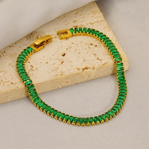 Close-up of emerald-cut green zircons set in a gold-plated tennis bracelet on stone