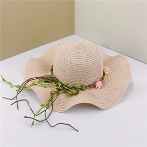 Detail of beige straw sun hat with wavy brim featuring pink roses and green leaves