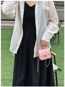 Close-up of pink quilted jelly bag with gold chain strap held by a model on green grass