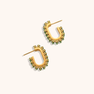 Vue macro de boucles d'oreilles dorées en U avec des zircons verts de coupe carrée