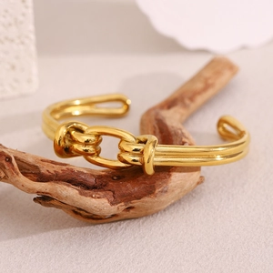 Detail of 18K gold-plated braided knot open cuff bracelet on a natural wood piece