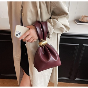Detail of burgundy ruched handbag featuring a luxury gold spherical metal handle clasp