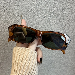 Close-up of tortoise shell rectangle sunglasses frame with dark lenses held by hand