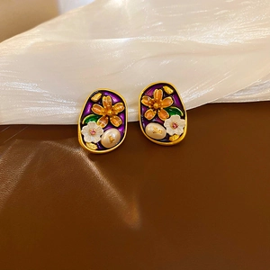 Close-up of vintage flower enamel earrings with pearls on brown leather background