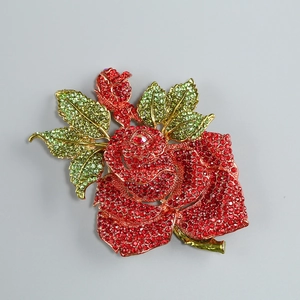 Détail d'une broche rose rouge avec strass incrustés et feuilles en cristal vert