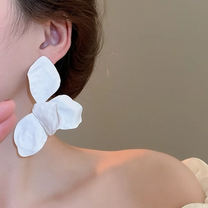 Close-up of white oversized matte flower petal earrings on a model with soft lighting