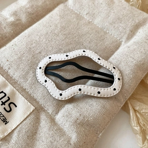 Macro shot of stylish wave-shaped hair clip with black polka dots on white matte surface
