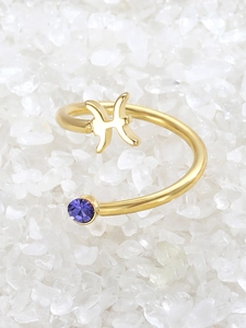 Detail of gold Pisces zodiac ring featuring a purple zircon stone on white pebbles