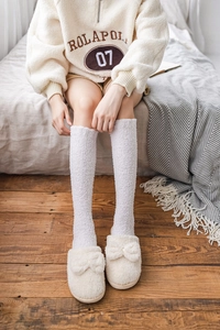 Close-up of soft white coral fleece over-knee socks worn by a model in a cozy bedroom