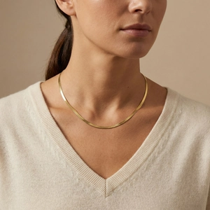 Close-up of a gold flat snake chain necklace with woven texture worn by a model