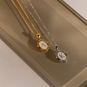 Gold A and silver K oval initial pendant necklaces displayed on a brown reflective tray