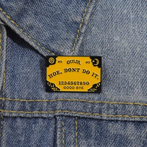 Épingle émaillée Ouija jaune avec lettrage noir fixée sur un tissu en jean bleu