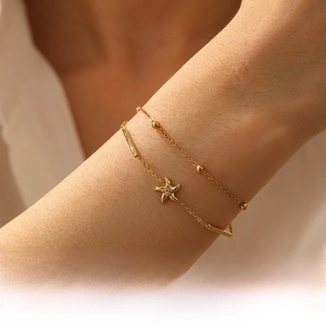 Close-up of gold plated layered chain bracelet featuring a zircon starfish charm on wrist