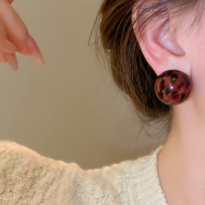 Close-up of a large tortoiseshell resin dome earring worn with a beige knit sweater