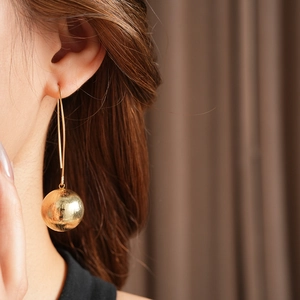 Détail de boucle d'oreille pendante dorée avec sphère en métal texturé sur un mannequin