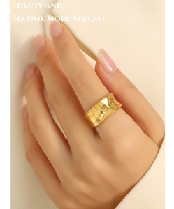 Close-up of golden wide band ring with irregular hammered texture on female index finger
