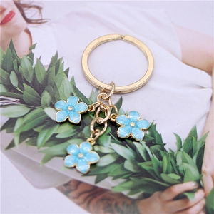 Close-up of golden keychain featuring three light blue enamel flower charms with gold centers