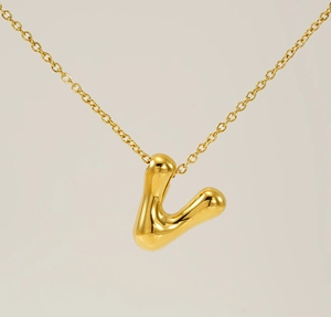 Macro view of polished golden bubble letter V pendant with shiny liquid metal texture