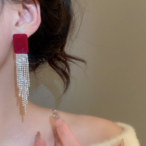 Dettaglio degli orecchini in velluto rosso con frange di strass lucenti sulla modella
