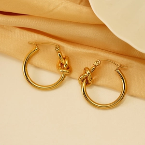 Polished gold titanium steel knot hoop earrings on soft silk background, elegant style