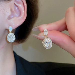 Detail view of oval gold earrings with a large clear center stone and micro-pave setting