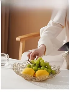 Golden mesh wire fruit basket with wavy edges holding fresh grapes and lemons on a table