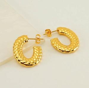 Macro detail of gold C-shape hoop earrings featuring a stylish hammered textured finish