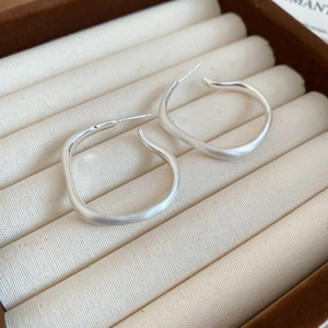 Detail view of irregular matte silver wavy hoop earrings on a beige velvet jewelry box