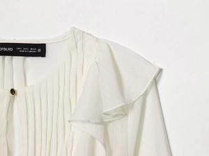 Detail of ruffled chiffon blouse featuring layered frills and a gold decorative button