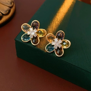 Close-up of golden floral earrings with colorful gemstones on a green jewelry box