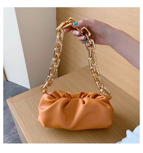 Detailed view of ginger orange cloud bag with a chunky gold chain strap on wood