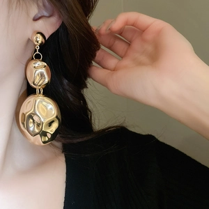 Close-up of golden irregular metal drop earrings with hammer texture on model
