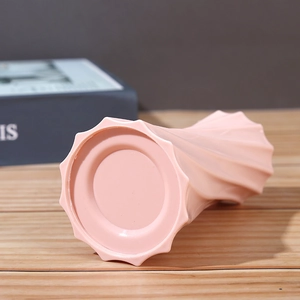 Pink Nordic ceramic vase with a unique wavy base design on a wooden tabletop